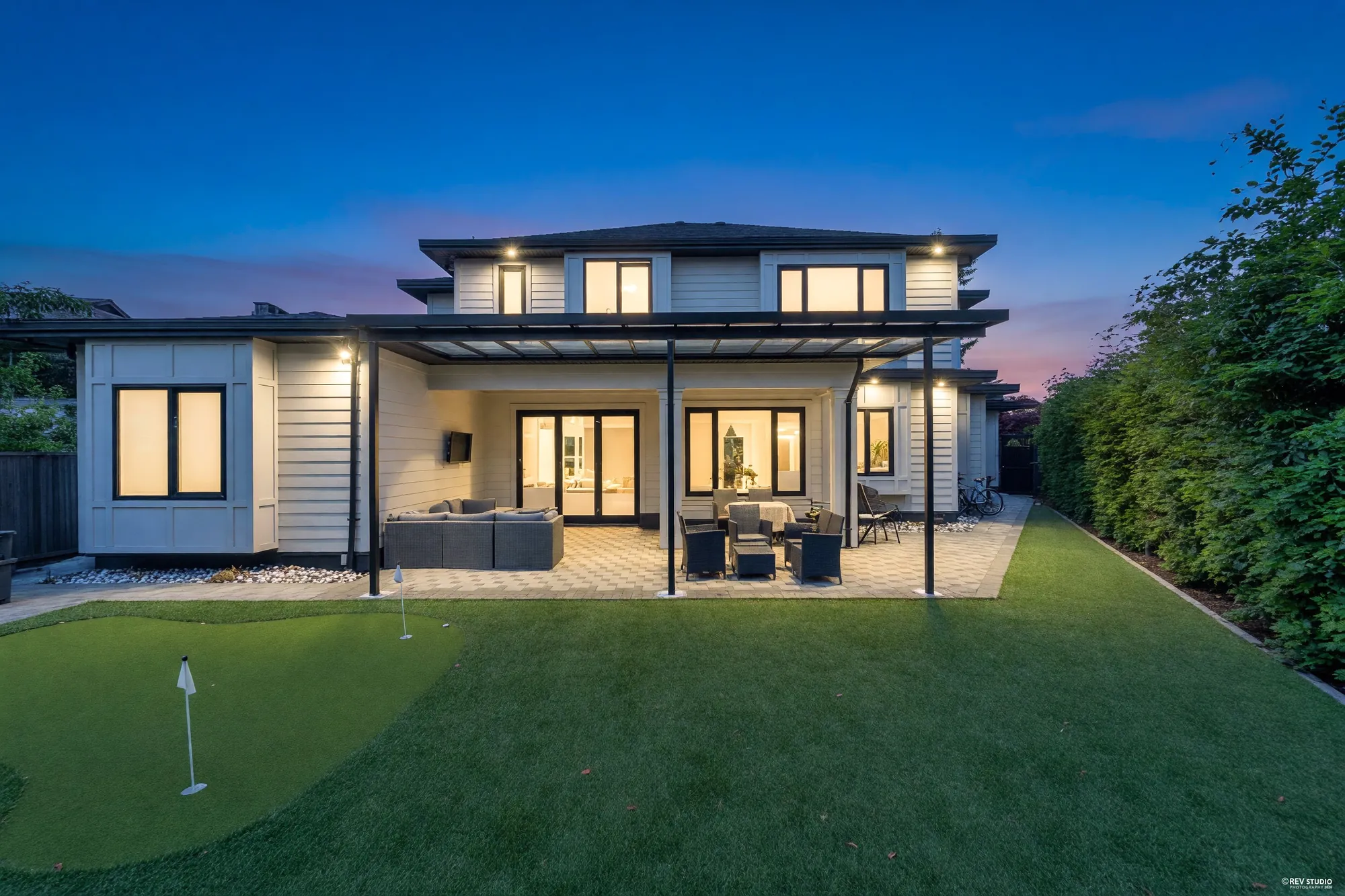 The same view of the back converted to dusk: the windows and the patio doors lit, lights under the eaves and the patio cover