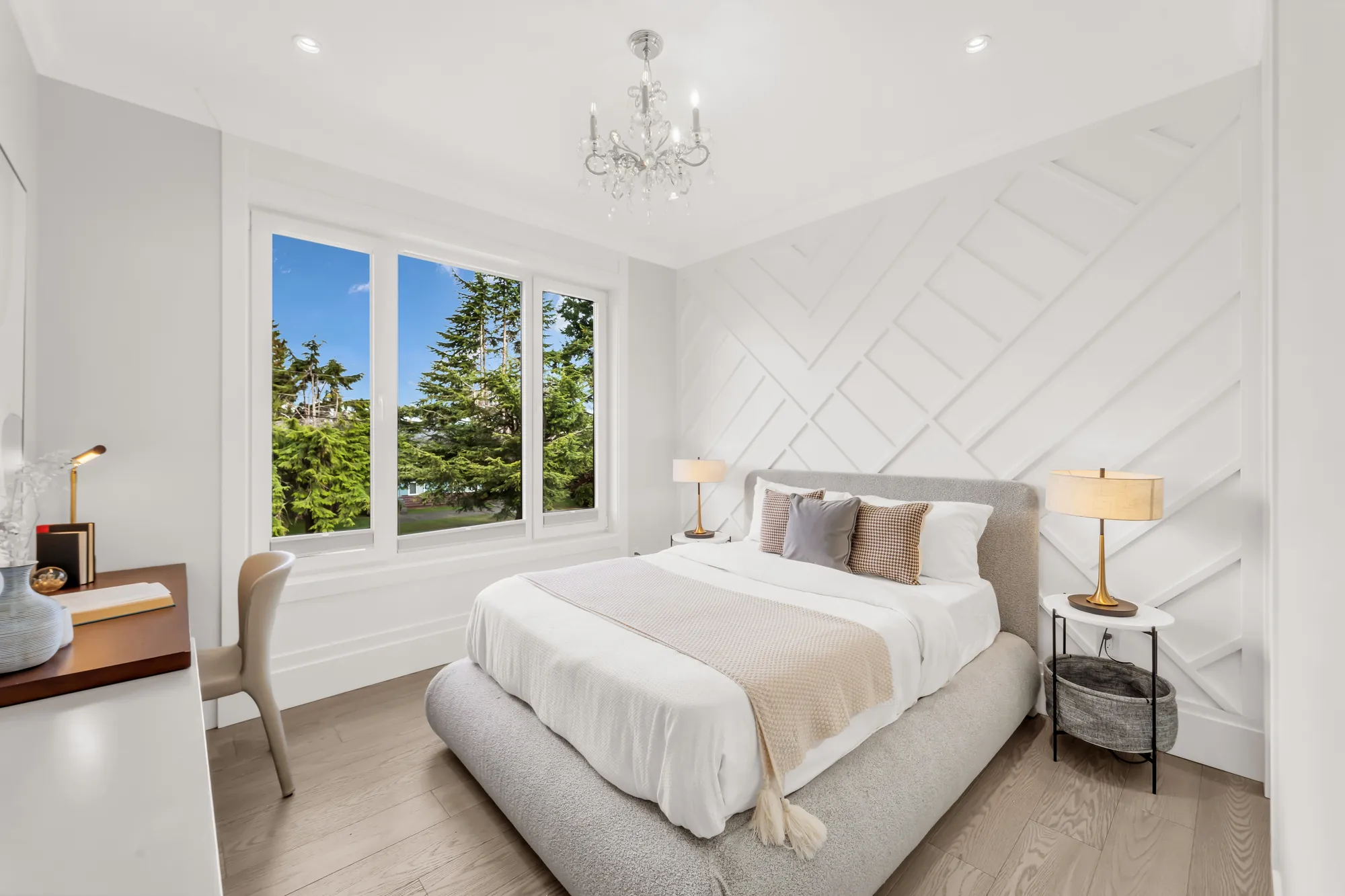 A bedroom with a white chevron-panelled wall: an upholstered bed, a window, a crystal chandelier, a desk and a chair