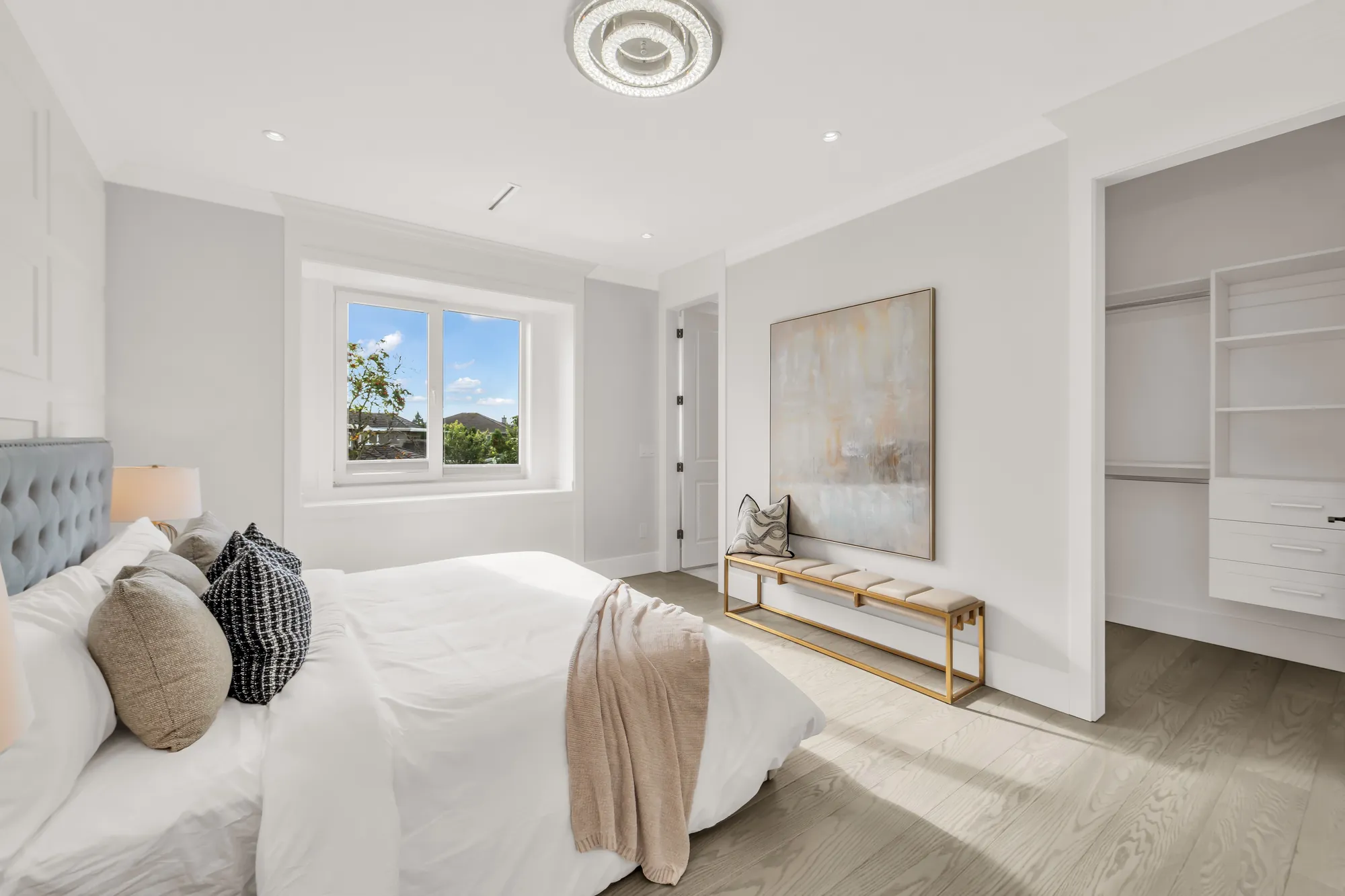 The same bedroom toward its walk-in closet, the bench and the painting, a window