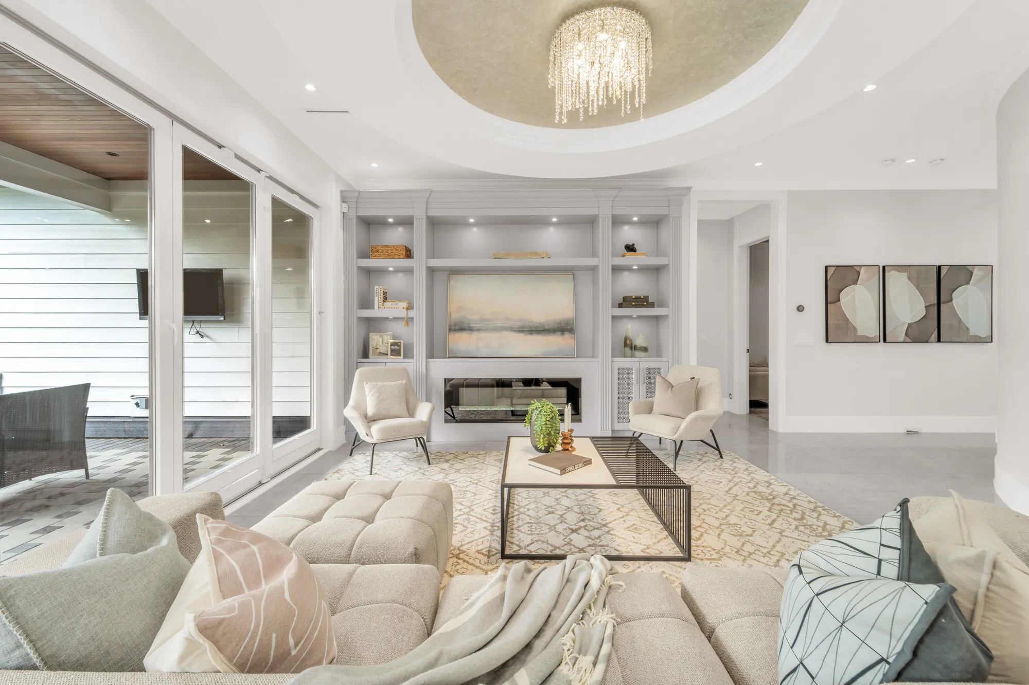 The family room beside a wall of sliding glass doors, the covered patio with its wood ceiling and television outside, the built-in shelving and the fireplace beyond