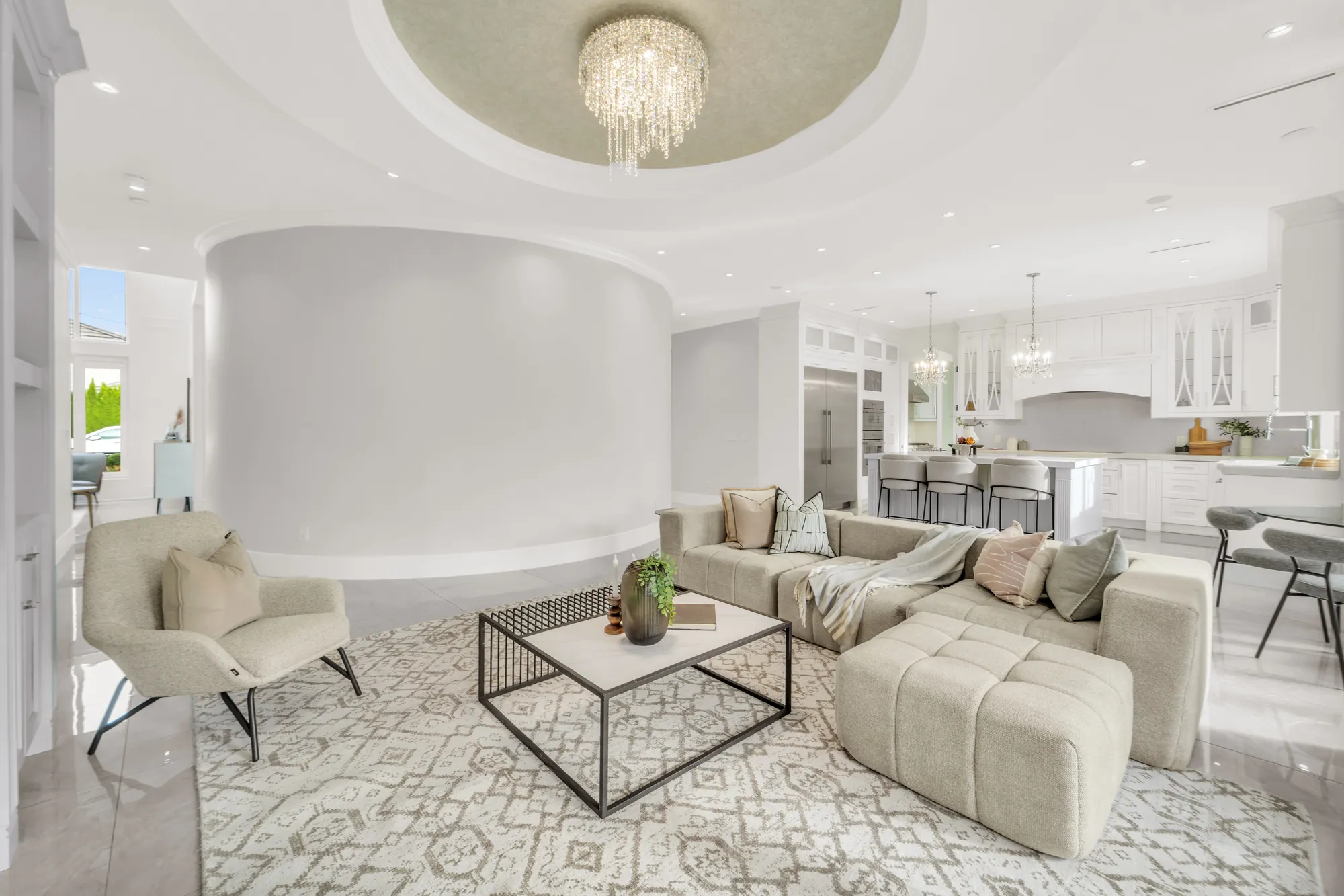 The family room toward the kitchen, past the curved wall: the island and stools, the stainless refrigerator and freezer columns, glass-front upper cabinets