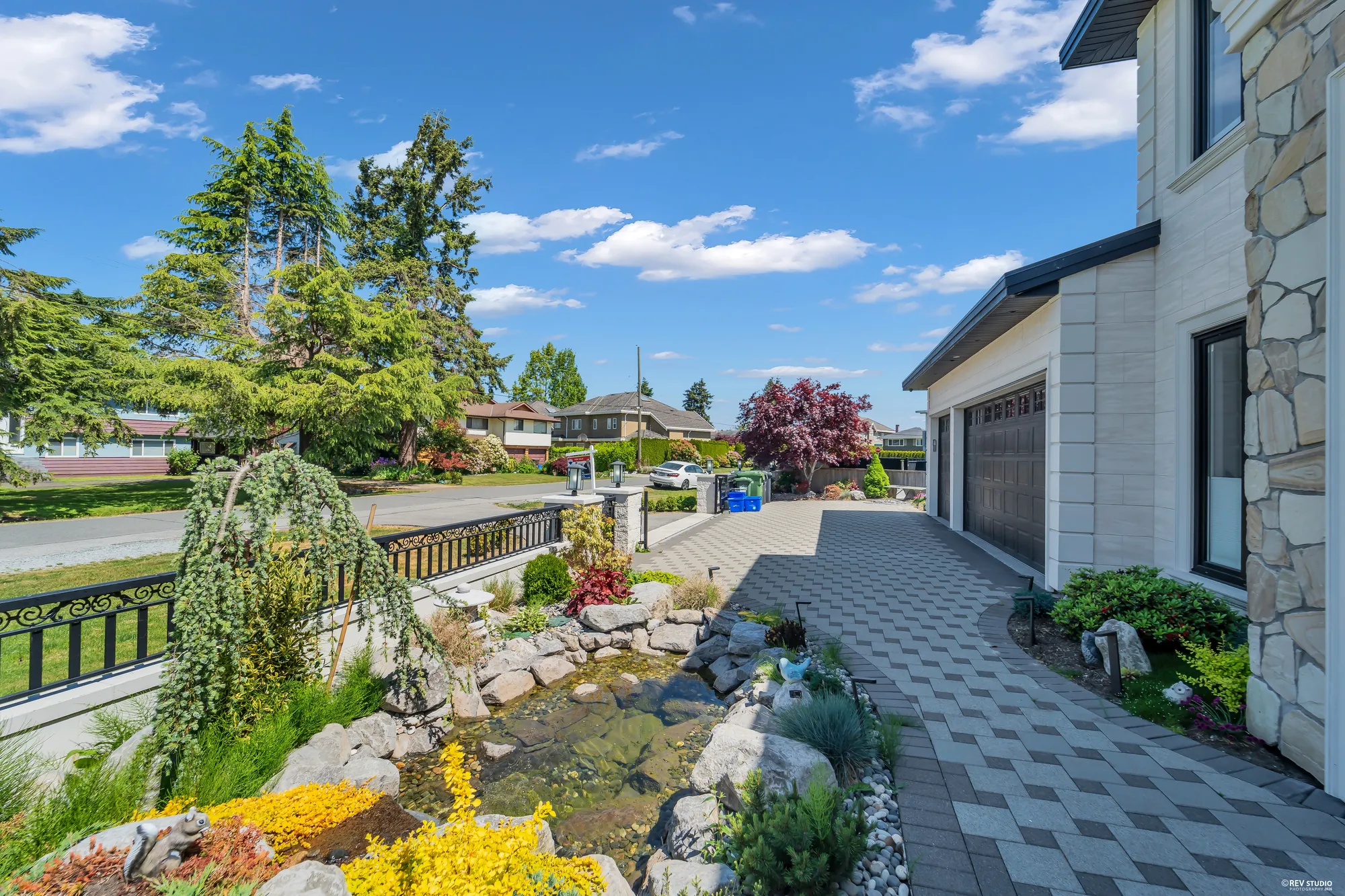 The front garden from beside the house: a weeping tree over the pond, rocks and flowering shrubs, the paver drive and the garage doors at the right