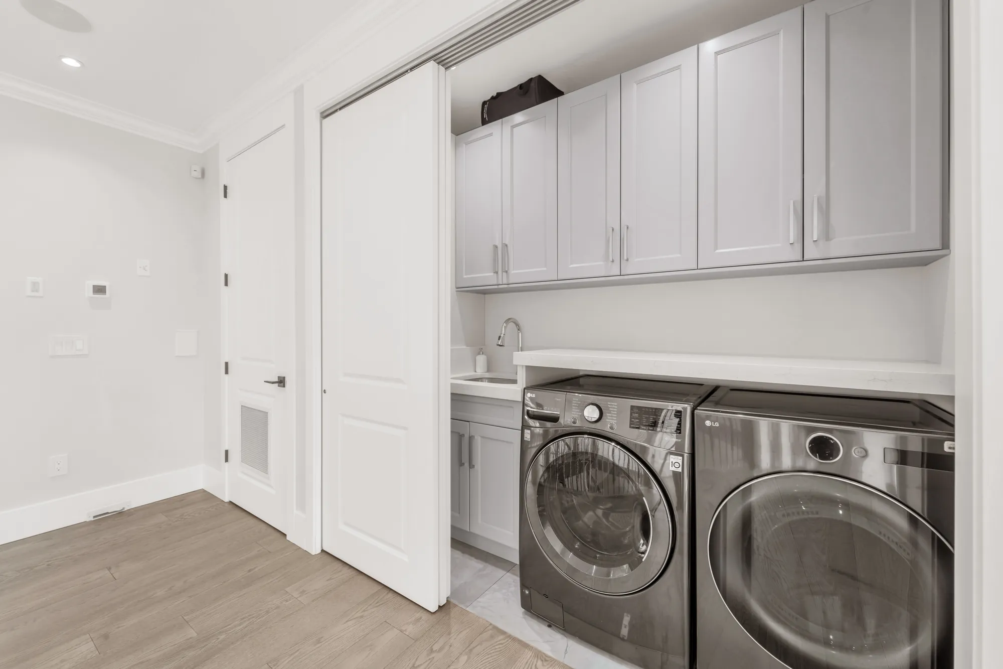 The laundry: a front-loading washer and dryer under white cabinets, a small sink, a sliding door