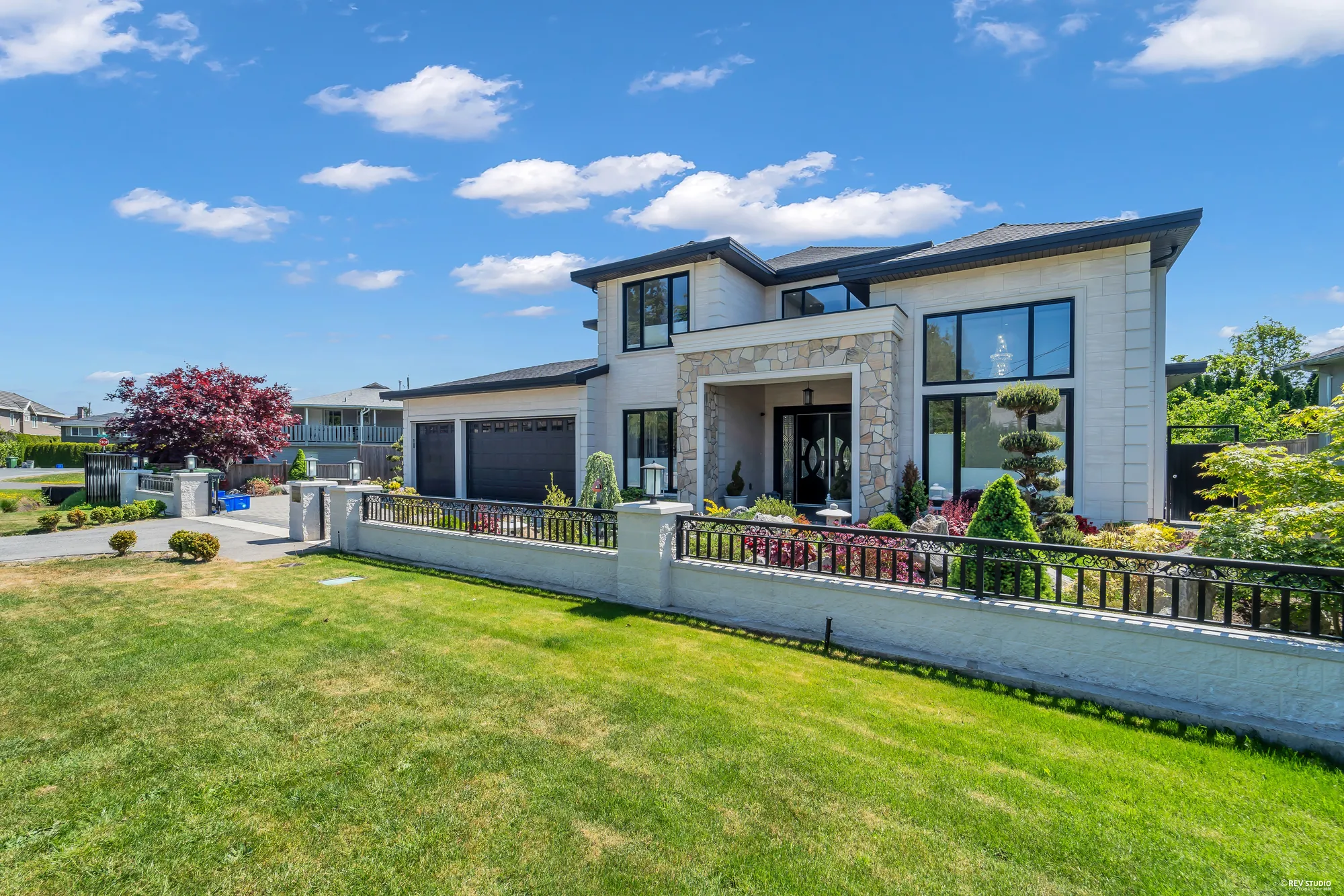 The front from the lawn at the right: the house behind the white wall and iron railing, a red Japanese maple at the left, clipped pines in the front garden, the lawn in front