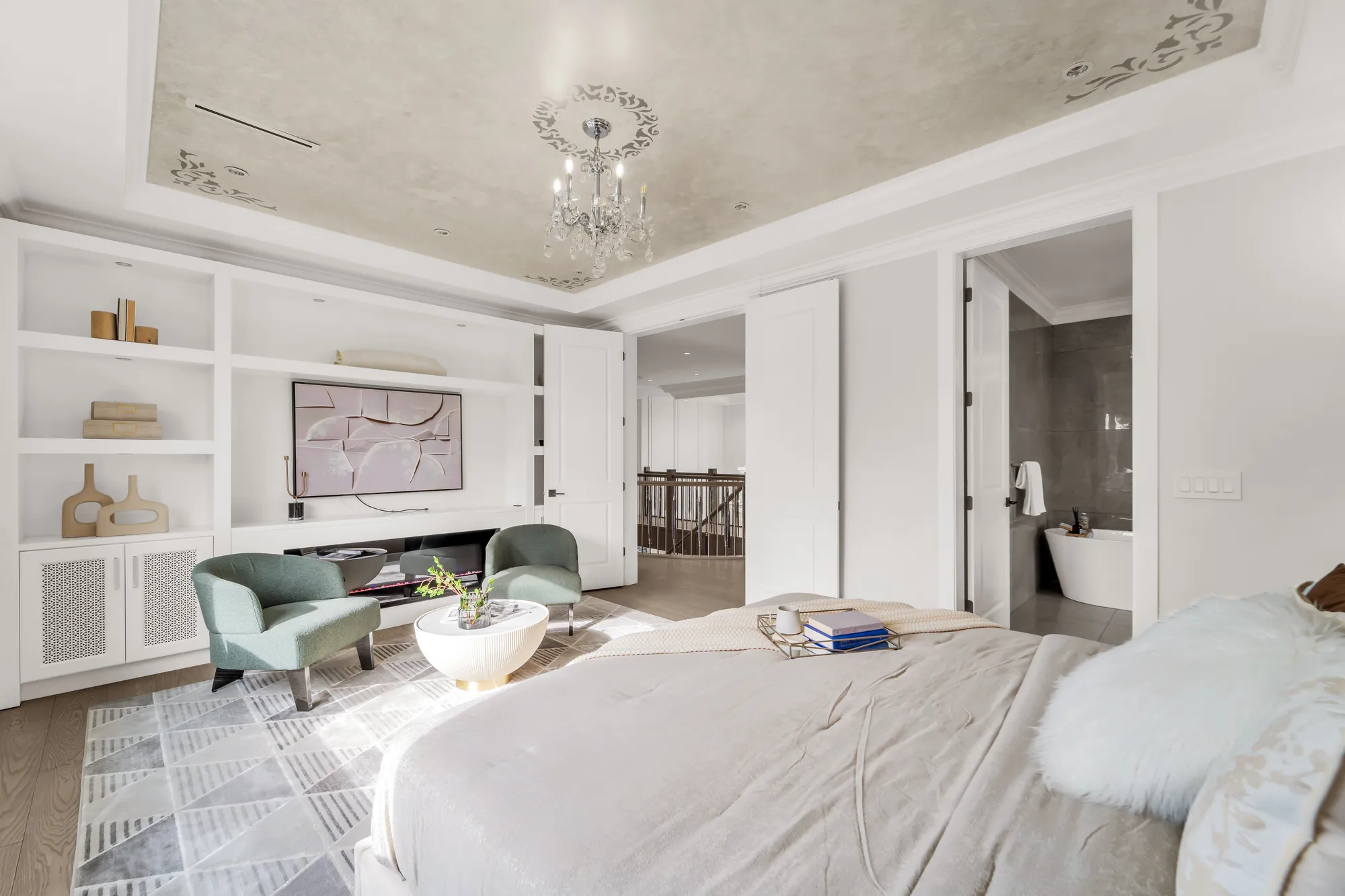 The primary bedroom toward its doors: the bathroom with a freestanding tub through the door at the right, the hall and the stair railing beyond