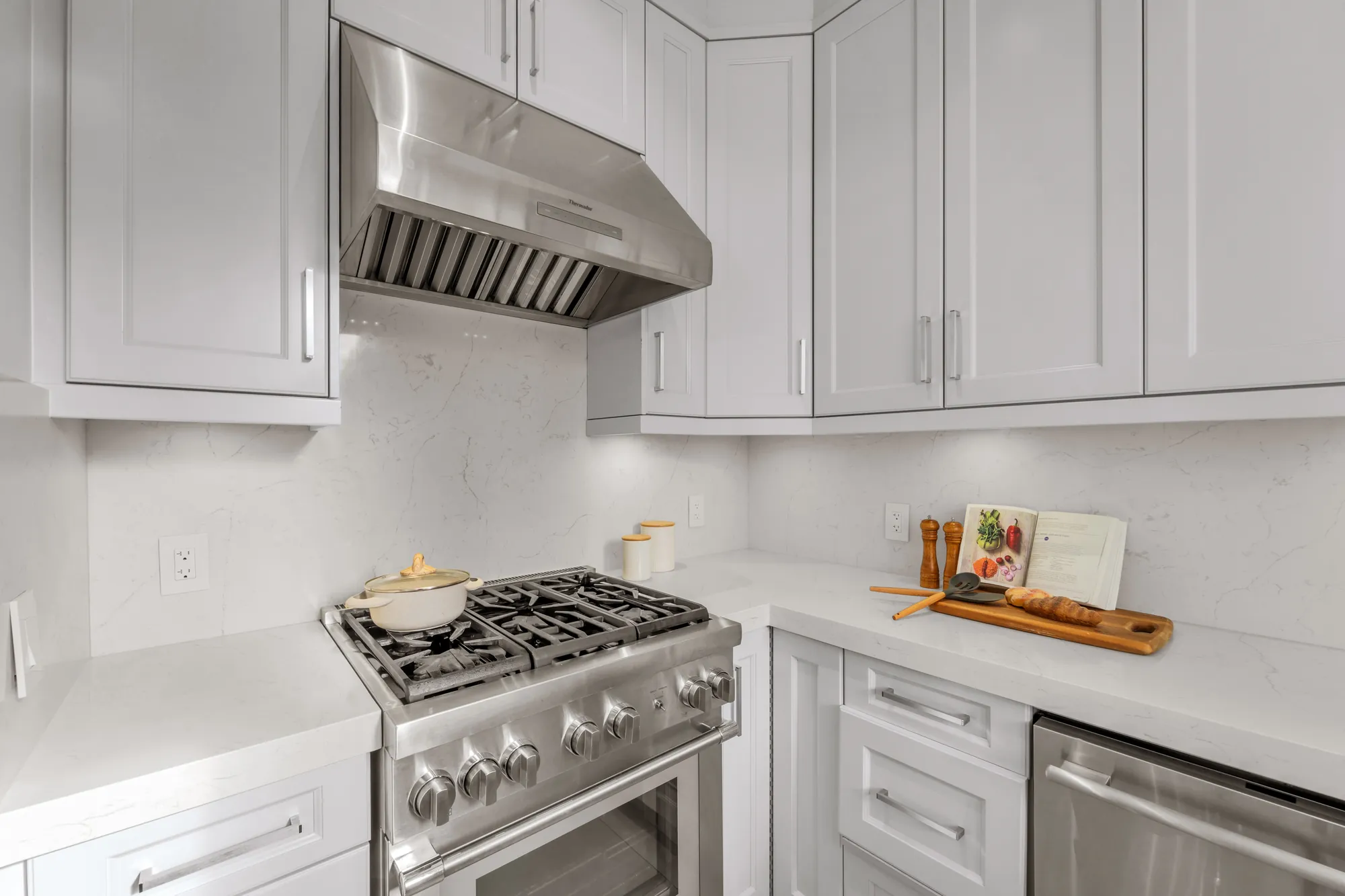 The stainless gas range in the second kitchen, four burners under a stainless hood, white cabinets, the dishwasher at the right